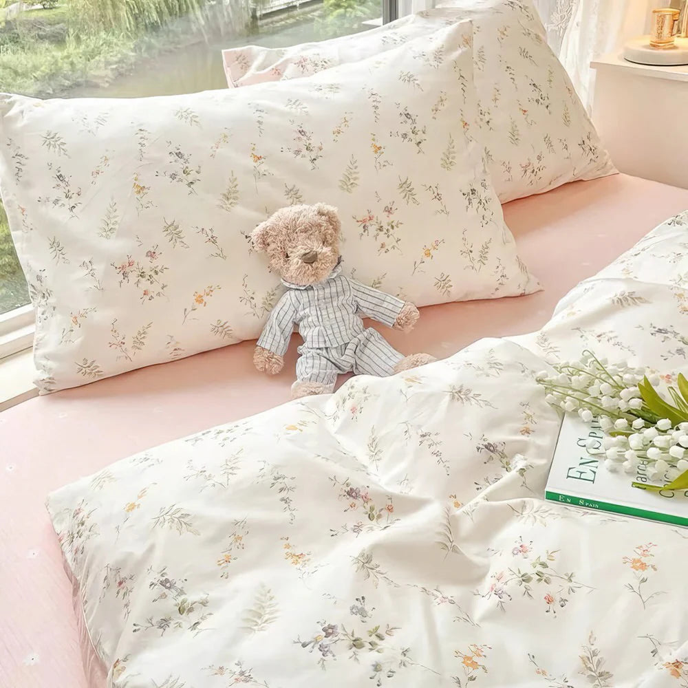 Floral-patterned pillows and a teddy bear on a pink bed with a window in the background