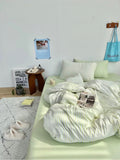 Neatly made bed with light green bedding in a room with a small table and decor items.