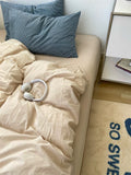 Beige bed with blue striped pillows and a white comforter, next to a nightstand.