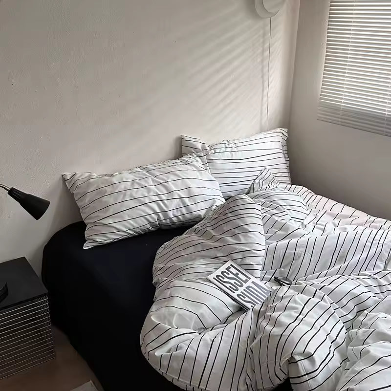 Bed with striped bedding and pillows in a room with a lamp and window.