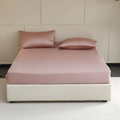 Pink bedspread and pillows on a bed against a beige wall.