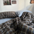 Plaid blanket draped over a bed with a visible brand label, in a bedroom setting.