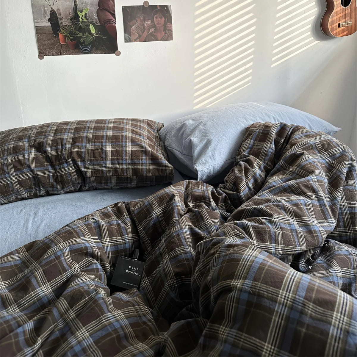 Plaid blanket draped over a bed with a visible brand label, in a bedroom setting.