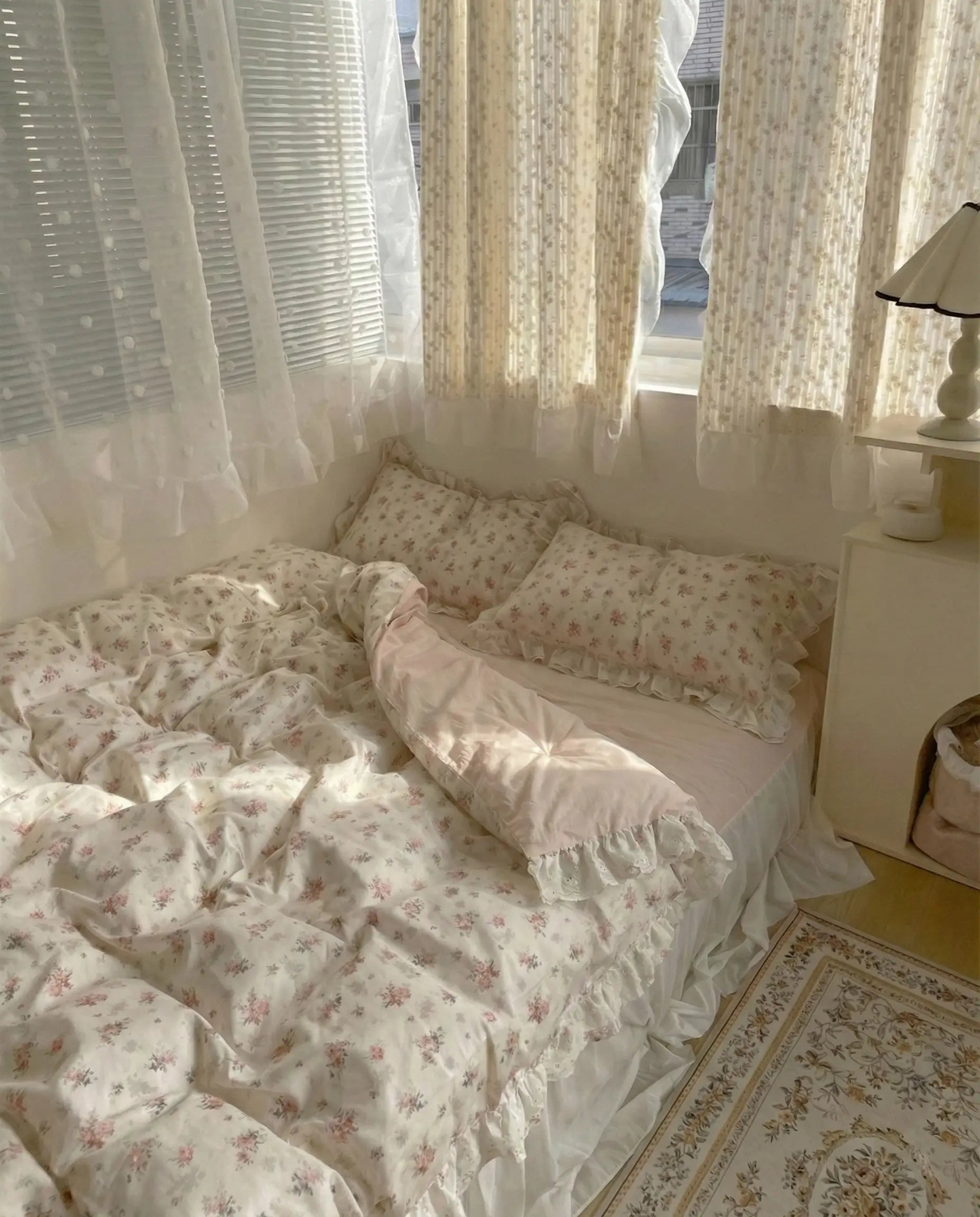 Bedroom with floral bedding and curtains, featuring a lamp on a nightstand.