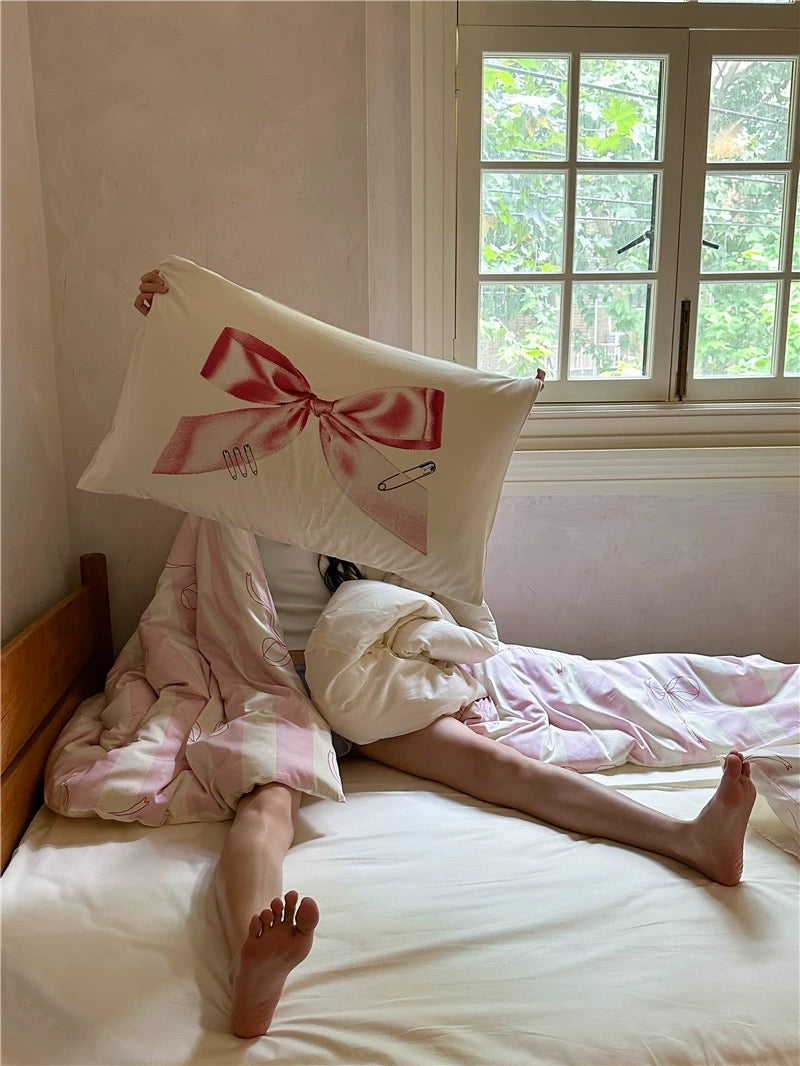 Two people under a pink blanket with a decorative pillow featuring a bow and hairpin design.