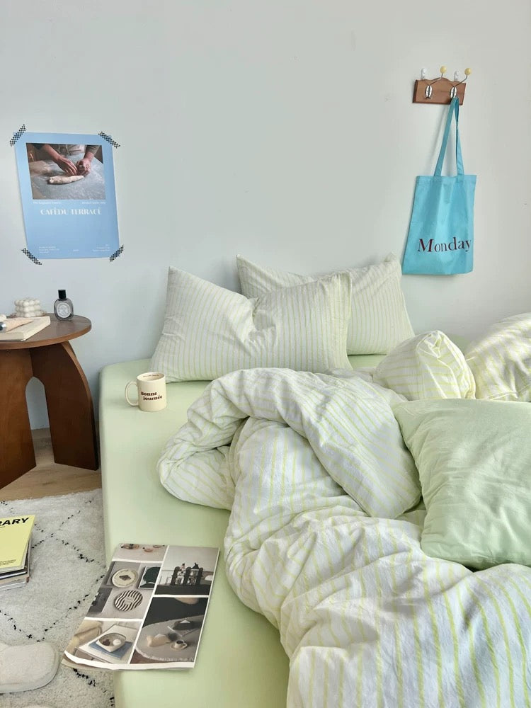 Bedroom with light green bedding and decor, including a tote bag and photo frame.