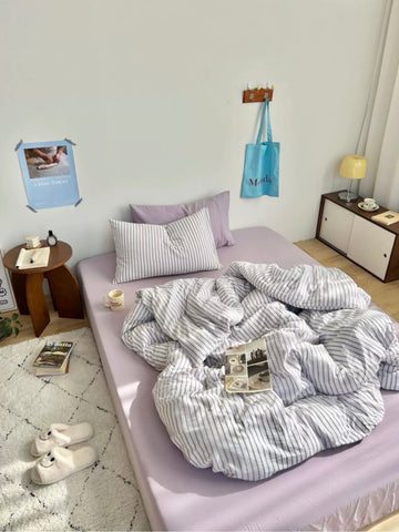 Bedroom with striped bedding and pillows on a bed, side table, and lamp.