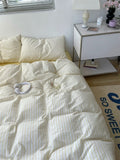Bed with white comforter and pillows in a room with a nightstand and lamp.