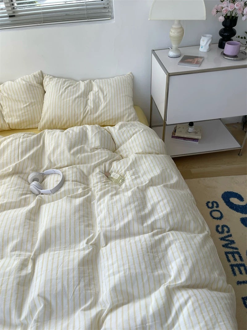 Bed with white comforter and pillows in a room with a nightstand and lamp.