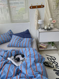 Bedroom with blue striped bedding, pillows, and a nightstand with books and a lamp.