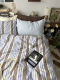 Bed with striped bedding and a tablet on a nightstand in a bedroom setting.