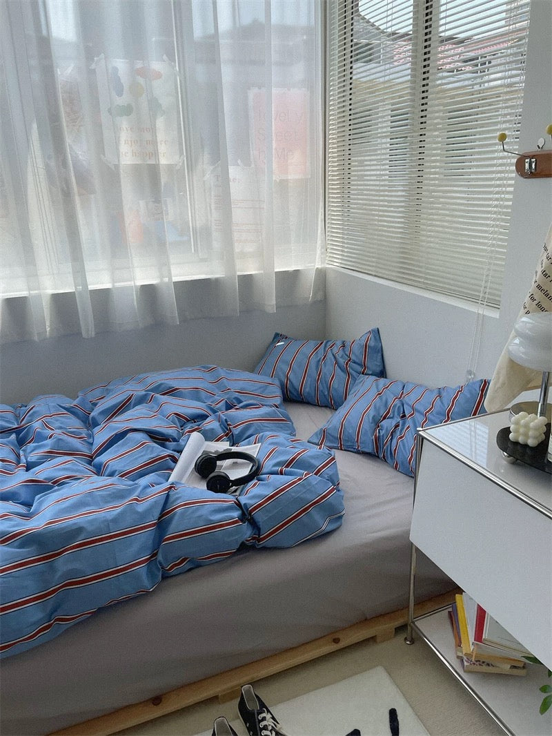 Bed with blue striped bedding in a room with large windows and a nightstand.