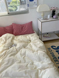 Bedroom with white comforter, red striped pillows, and a nightstand with lamp and decor items.
