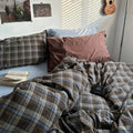 Bed with plaid bedding and pillows, book, and plant in a room.