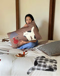 Woman holding a pillow with cartoon cat design on a bed with similar patterned pillows.