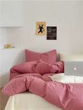 Bed with pink striped bedding and pillows, white walls with framed art, and a laptop on the bed.