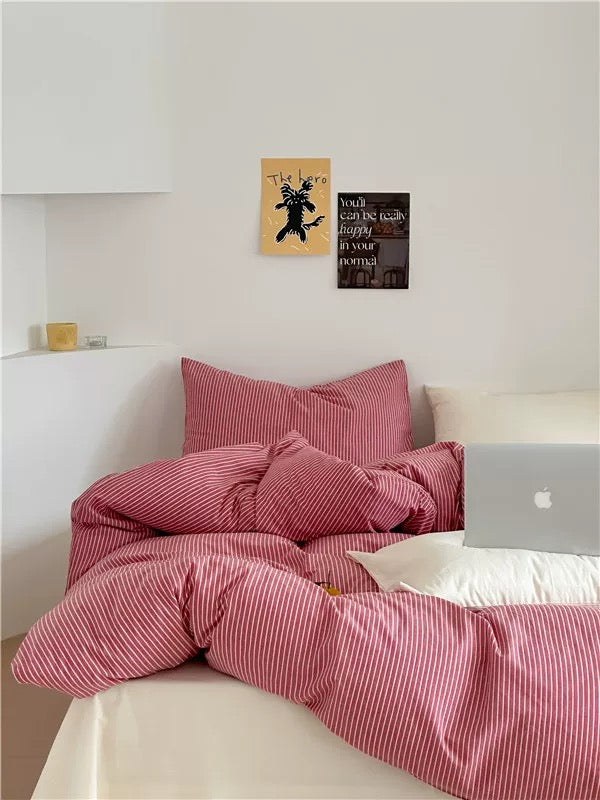 Bed with pink striped bedding and pillows, white walls with framed art, and a laptop on the bed.