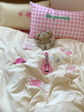 Children's bedroom with pink checkered pillow, teddy bear, and decorative elements on a white bedspread.
