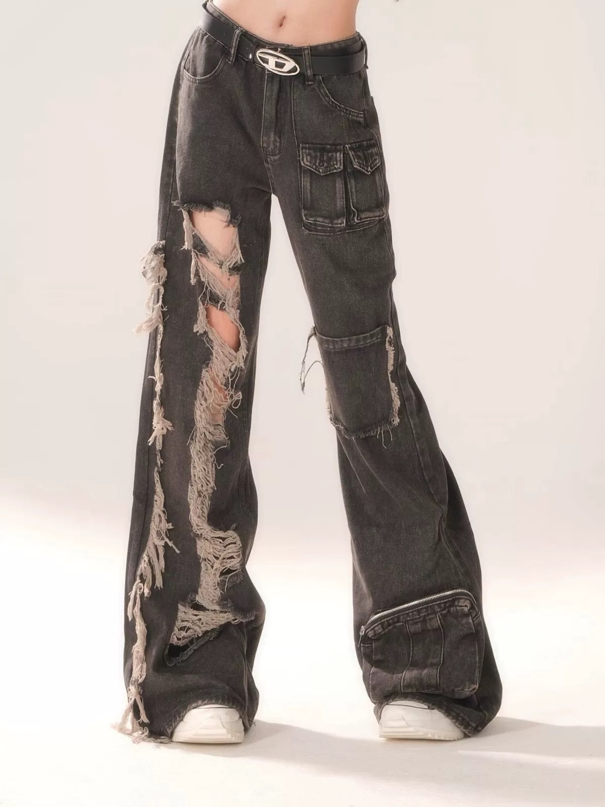 Side profile highlighting the baggy fit and hollow-out rips on the black denim trousers.